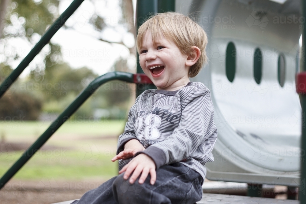Toddler boy laughing at top of playground equipment - Australian Stock Image