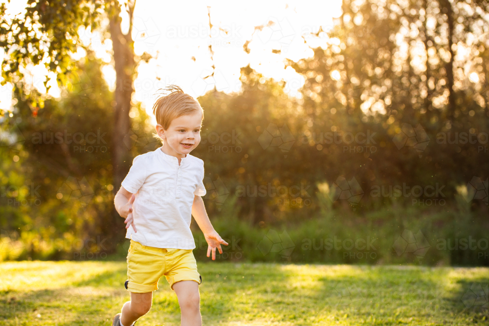 Toddler boy running through parkland in golden light with bokeh backdrop copy space - Australian Stock Image