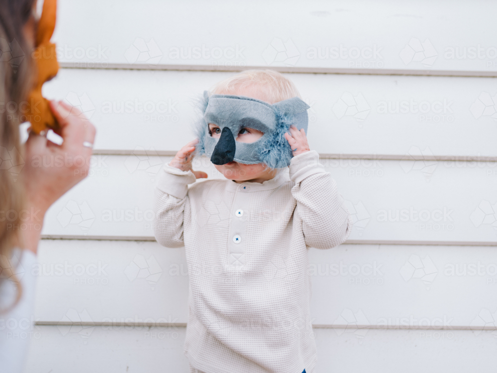 Toddler boy wearing koala mask standing against a white wall - Australian Stock Image