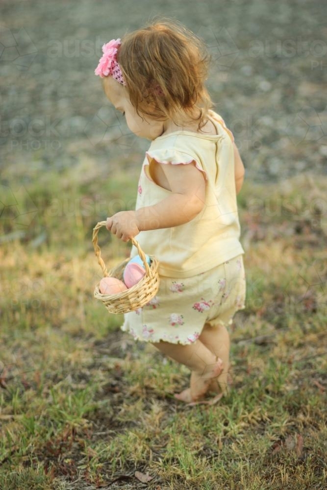 Toddler carrying a basket of easter eggs - Australian Stock Image