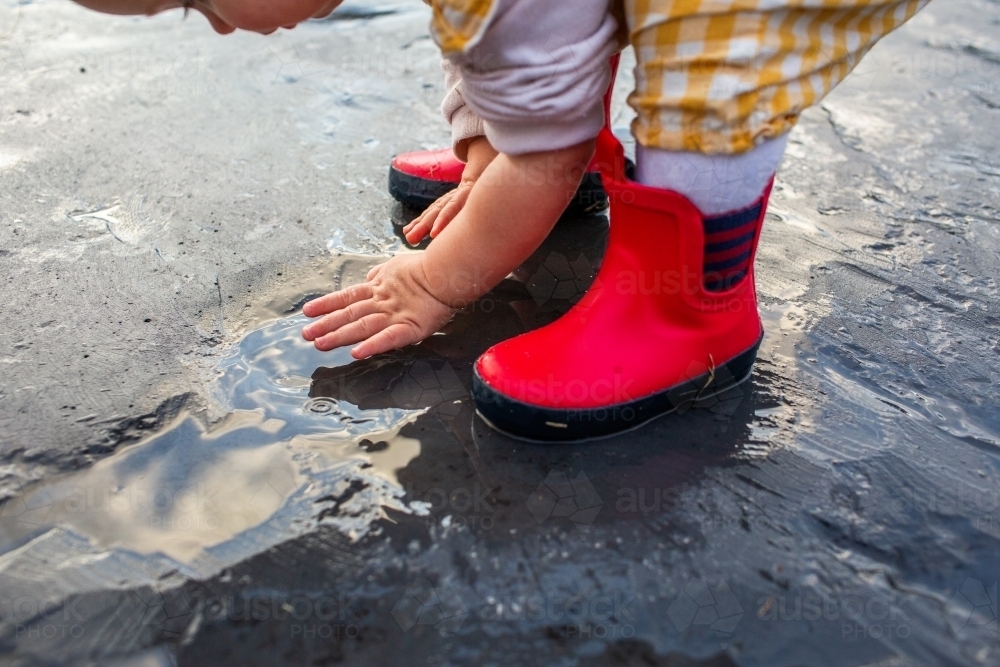 Toddler child in gumboots splashing in rainwater on urban driveway - Australian Stock Image