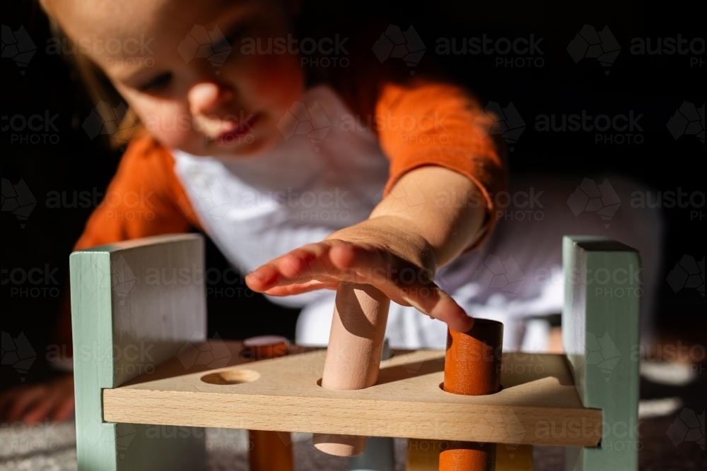 Toddler child playing with hammer pounding bench toy using hands to press blocks - Australian Stock Image