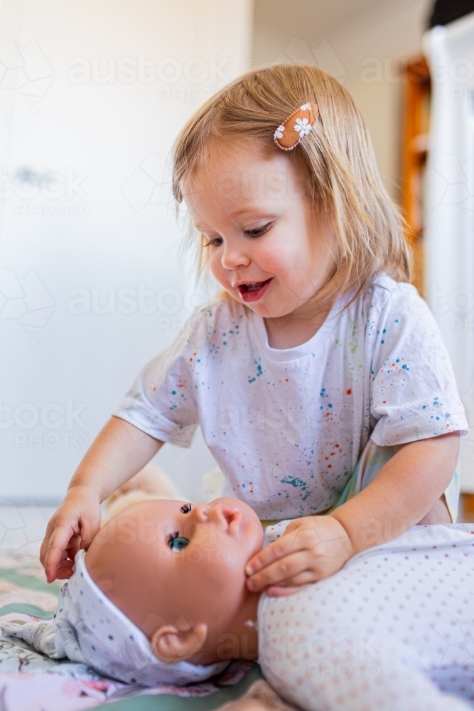 Toddler child playing with toy dolly on floor - Australian Stock Image