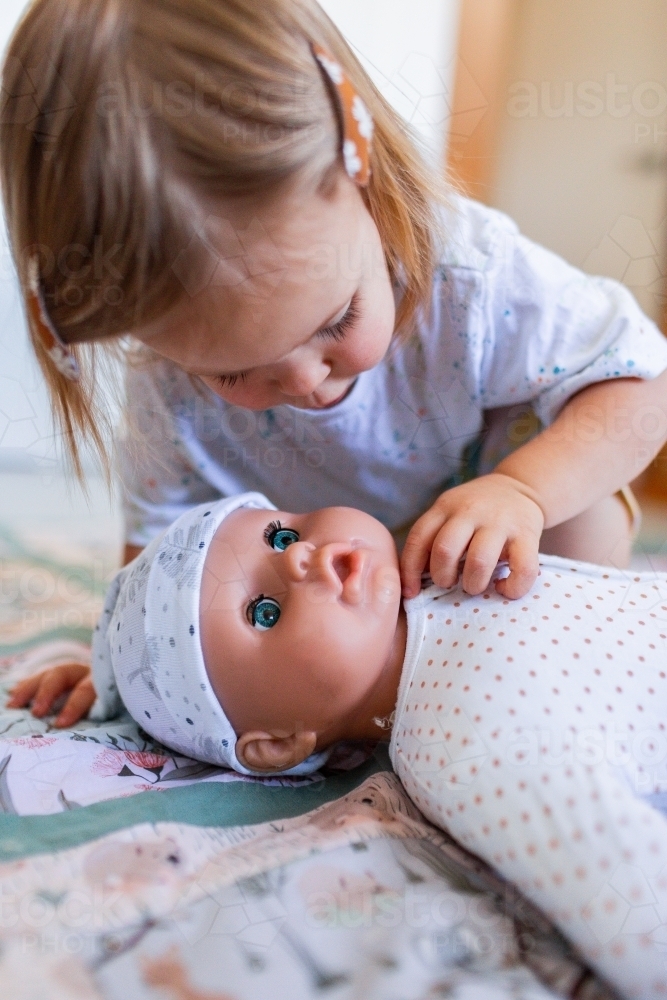 Toddler child playing with toy dolly on floor - Australian Stock Image