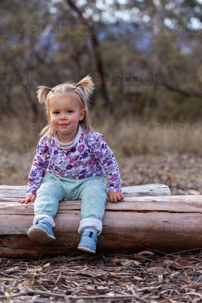 Image of Toddler child sitting on log in bushland camping area ...