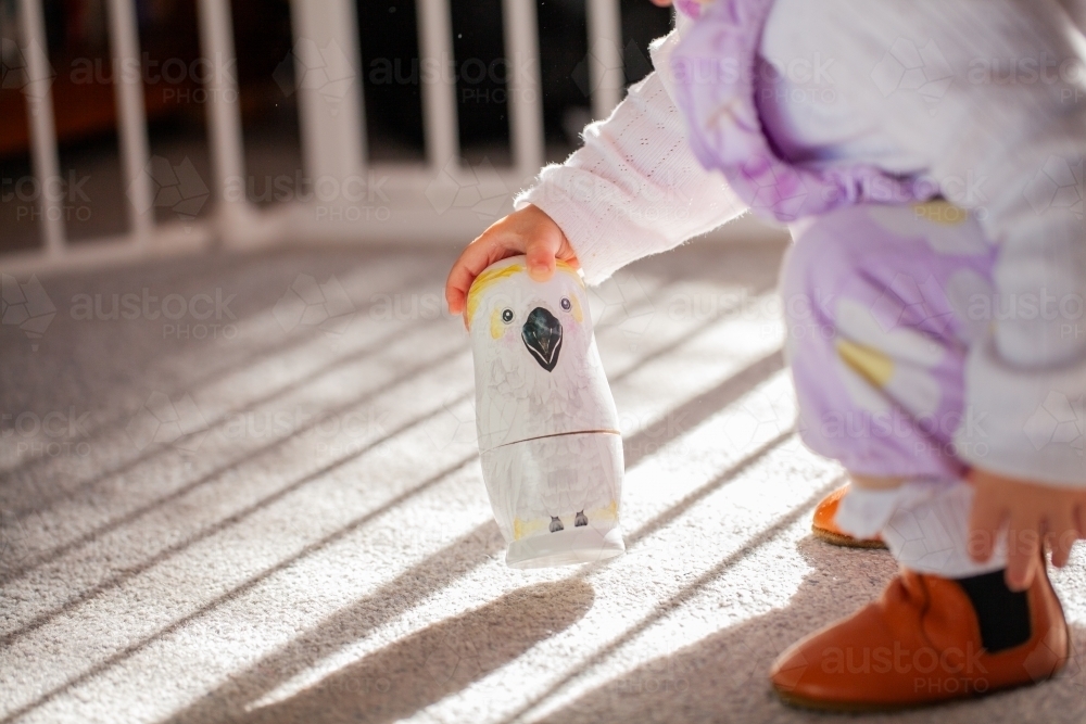 Toddler girl child playing on floor inside home with australian bird babushka nesting dolls - Australian Stock Image