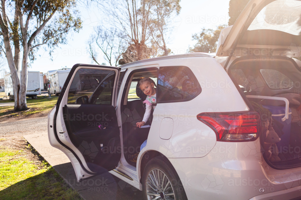 toddler girl climbing into car seat ready for holiday trip adventure - Australian Stock Image