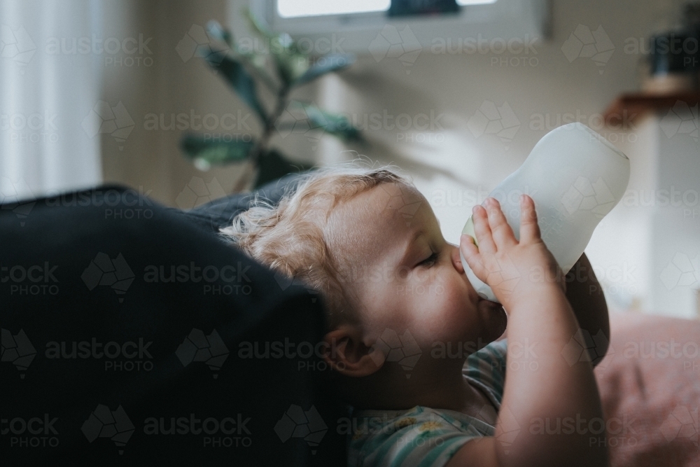 Toddler girl drinking milk from morning bottle - Australian Stock Image