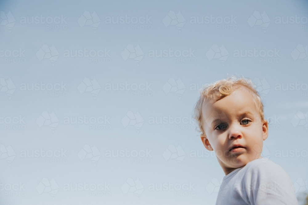Toddler girl looking down framed by blue sky - Australian Stock Image