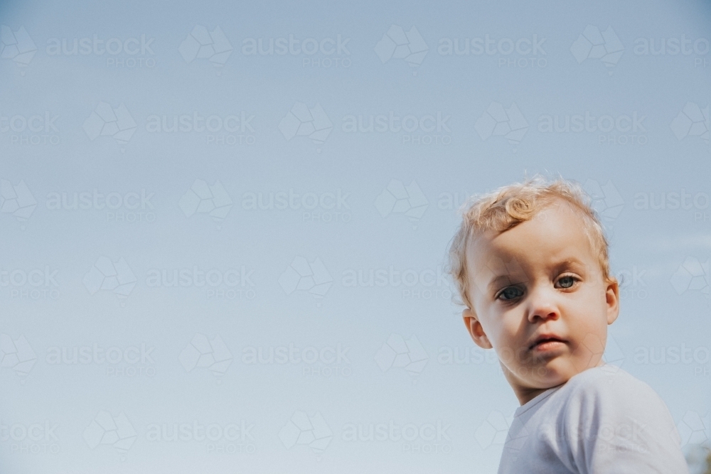 Toddler girl looking straight at the camera framed by blue sky - Australian Stock Image