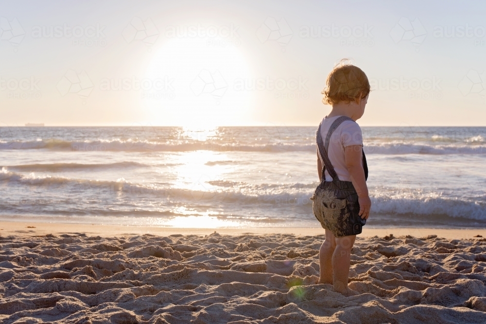 Toddler Girl On The Beach Looking Away Out To The Ocean At Sunset - Australian Stock Image