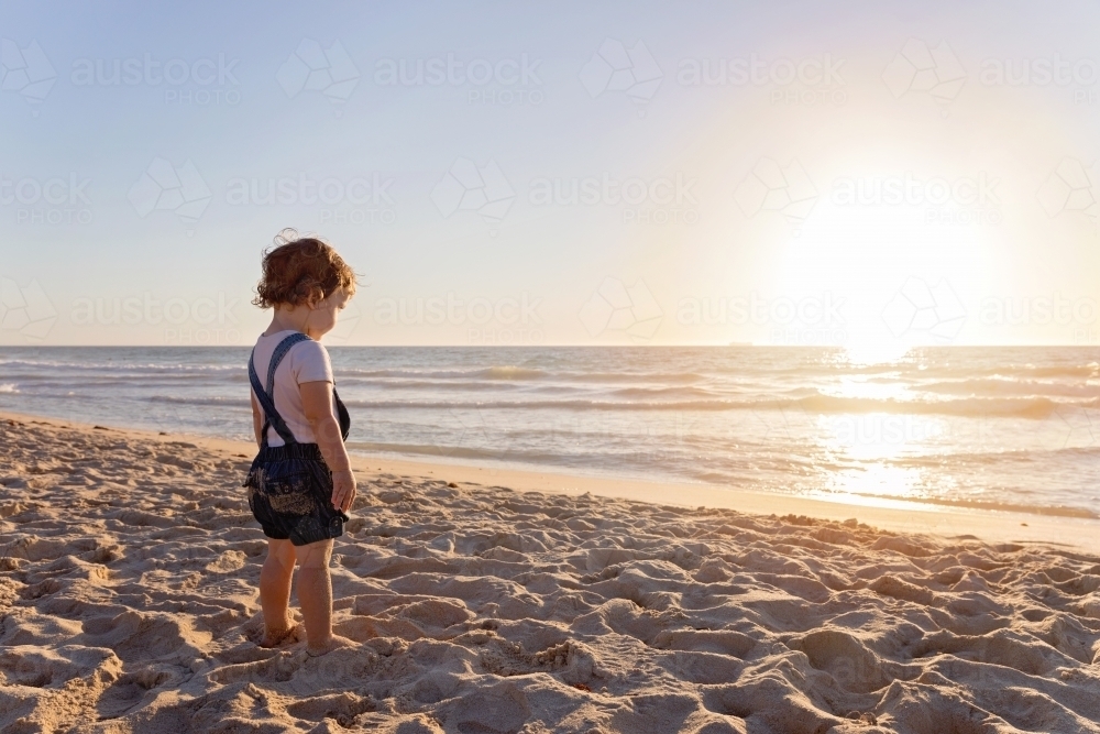 Toddler Girl On The Beach Looking Out To The Ocean At Sunset - Australian Stock Image