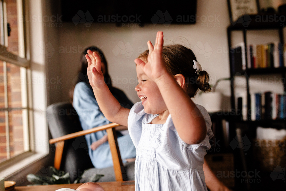 Toddler girl putting hands up in the air happily. - Australian Stock Image