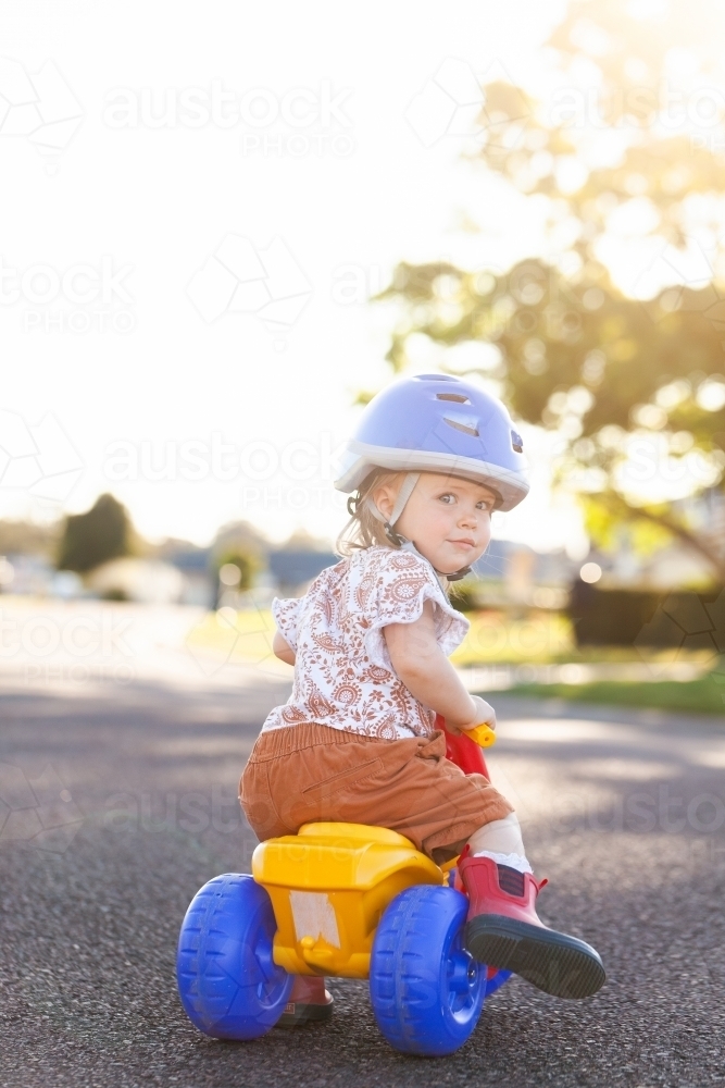 Image of Toddler girl riding trike on quiet suburban road wearing bike ...