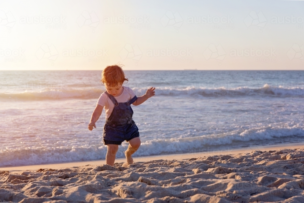 Toddler Girl Running On The Beach At Sunset Looking Down At The Sand - Australian Stock Image