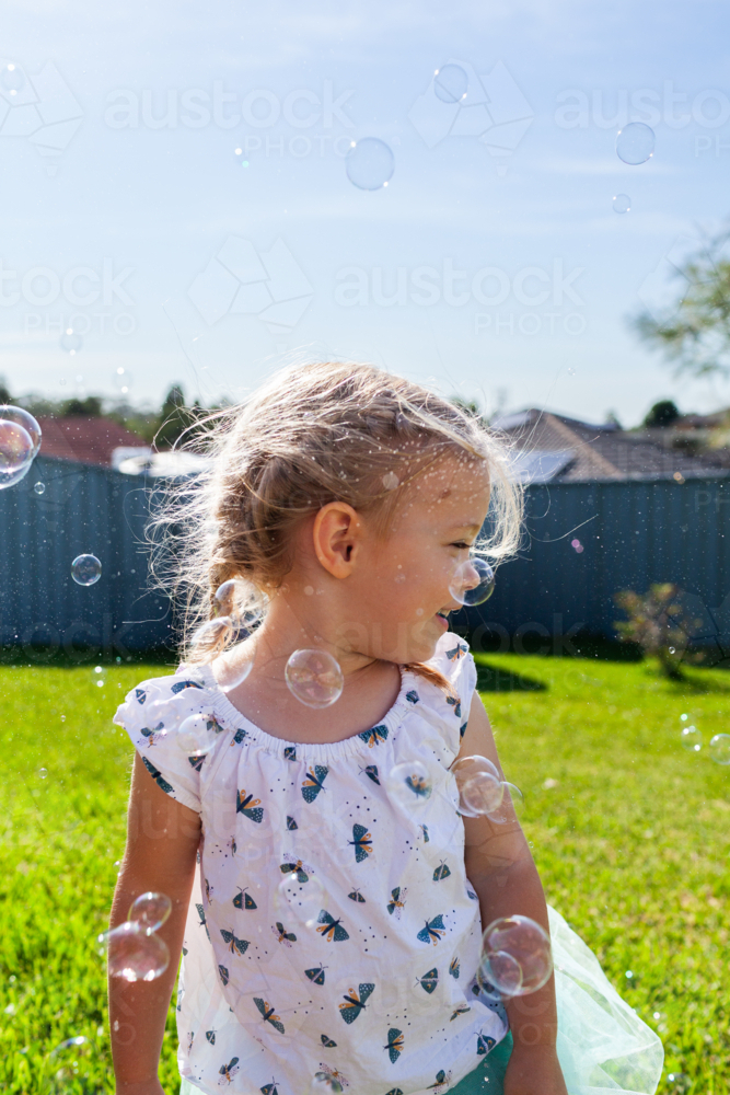 Toddler girl side profile playing in backyard with sparkling bubbles - Australian Stock Image