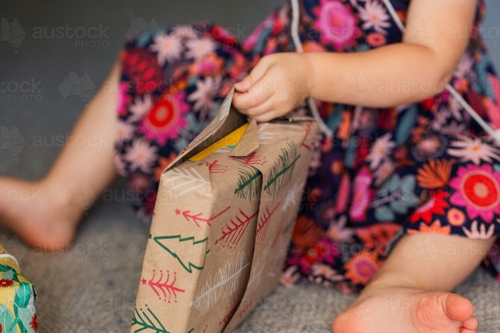 Toddler girl unwrapping gift tied with string - Australian Stock Image