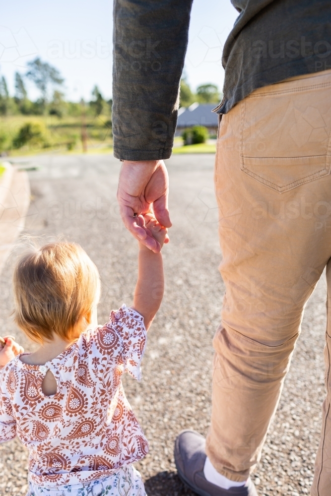 Toddler girl walking on road holding parents hand - Australian Stock Image