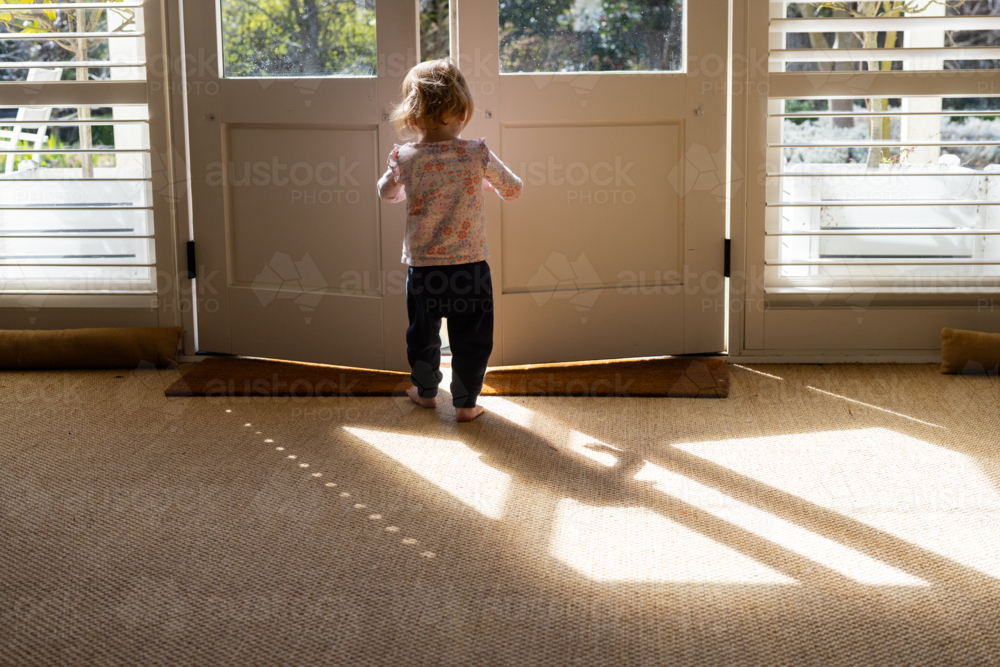 Toddler girl walking out of the door to the garden - Australian Stock Image
