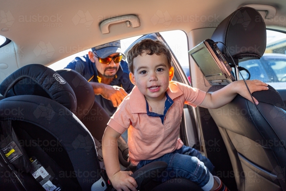 toddler in back seat of car with father leaning in the door - Australian Stock Image