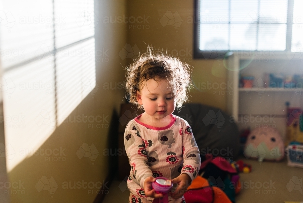 Toddler in sun flare playing with toys - Australian Stock Image
