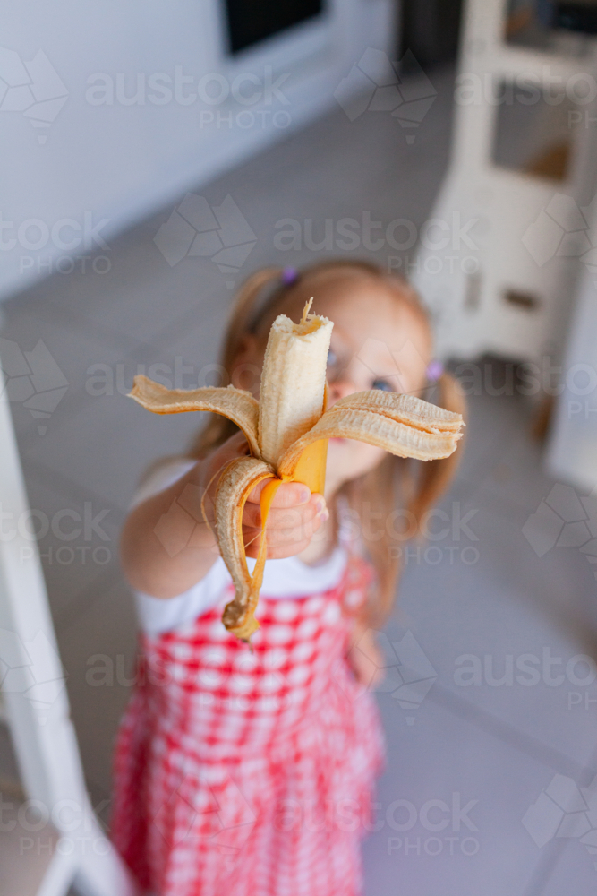 Toddler kid holding up banana with bite taken out of it inside home - Australian Stock Image