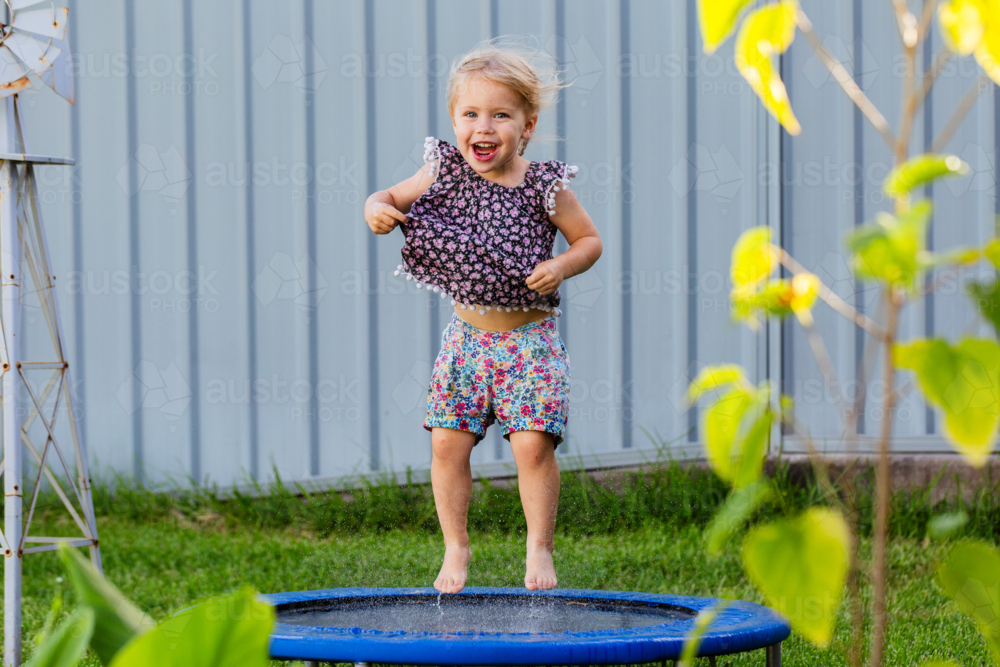 Toddler kid playing outside jumping on mini trampoline in backyard of home - Australian Stock Image
