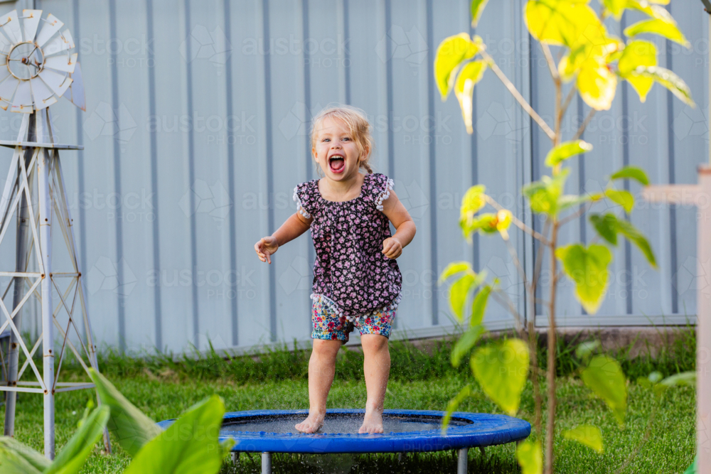 Toddler kid playing outside jumping on mini trampoline in backyard of home - Australian Stock Image