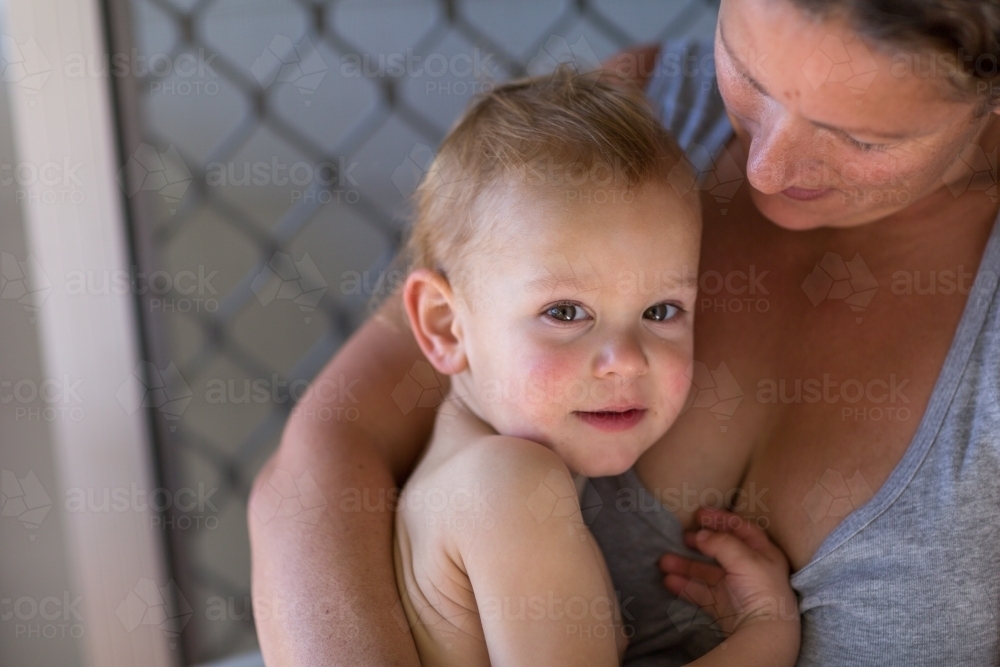 Toddler looking at camera, held in his mother's arms - Australian Stock Image