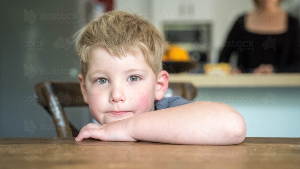 Toddler looking at camera leaning on table - Australian Stock Image
