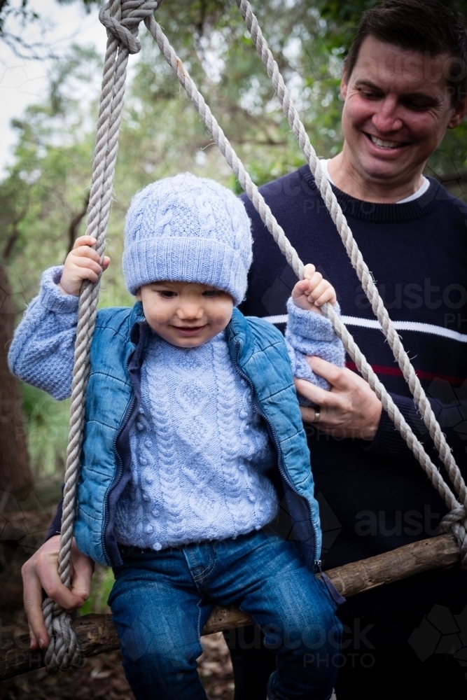 Toddler on rustic swing with father in bush setting - Australian Stock Image