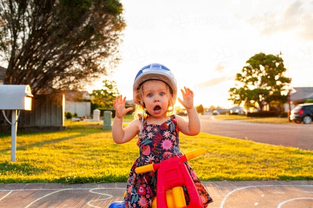 Toddler on trike with open mouthed shock expression wearing helmet - Australian Stock Image