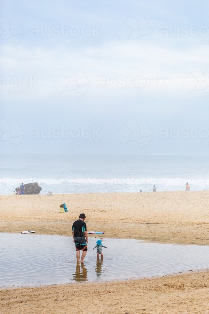 Toddler playing in tide pool with dad at Redhead beach on overcast day - Australian Stock Image