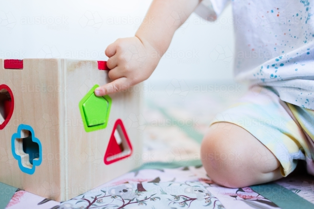 Toddler posting coloured shapes into wooden shape sorter box - Australian Stock Image