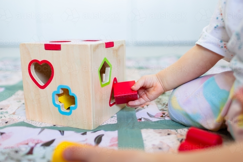 Image of Toddler posting coloured shapes into wooden shape sorter box ...