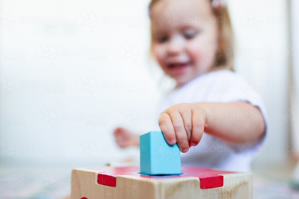 Image of Toddler posting coloured shapes into wooden shape sorter box