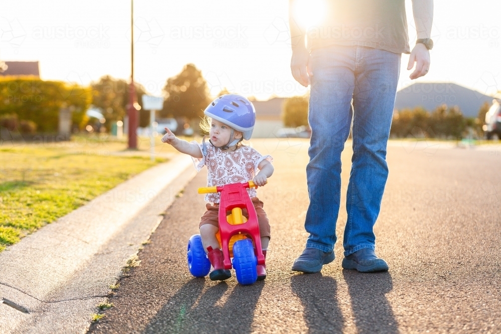 Image of Toddler riding on tricycle bike down suburban road on walk