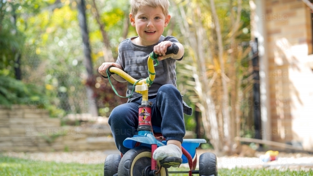 Toddler riding tricycle in backyard - Australian Stock Image
