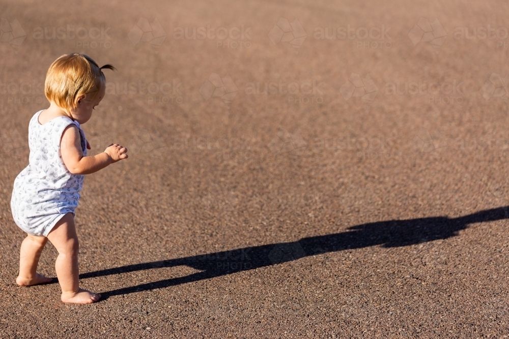 Toddler with long shadow walking across road - Australian Stock Image