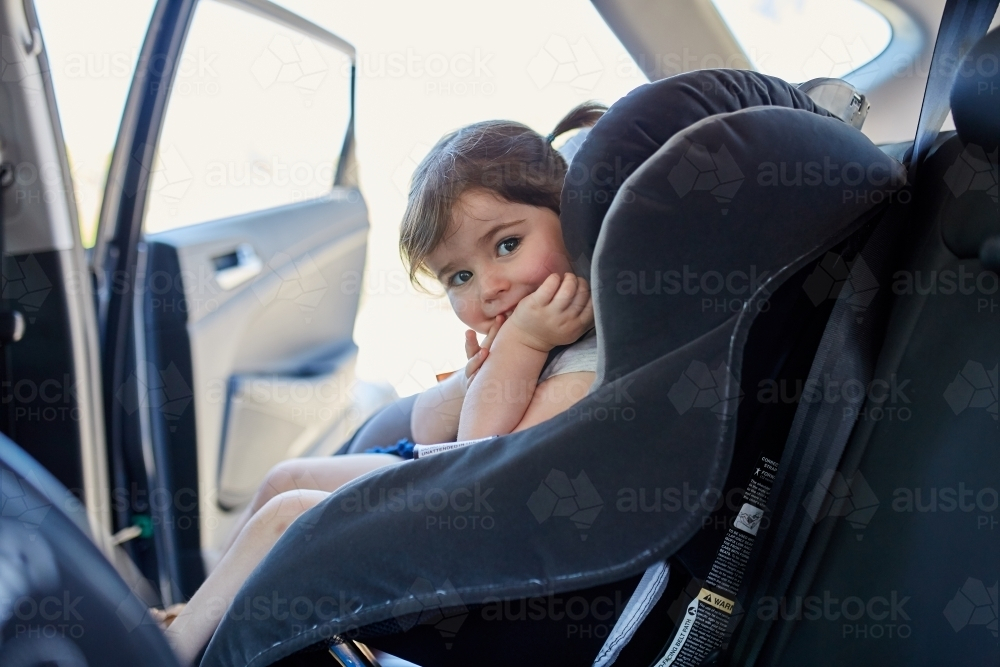 Toddler with pigtails sitting in child car seat - Australian Stock Image