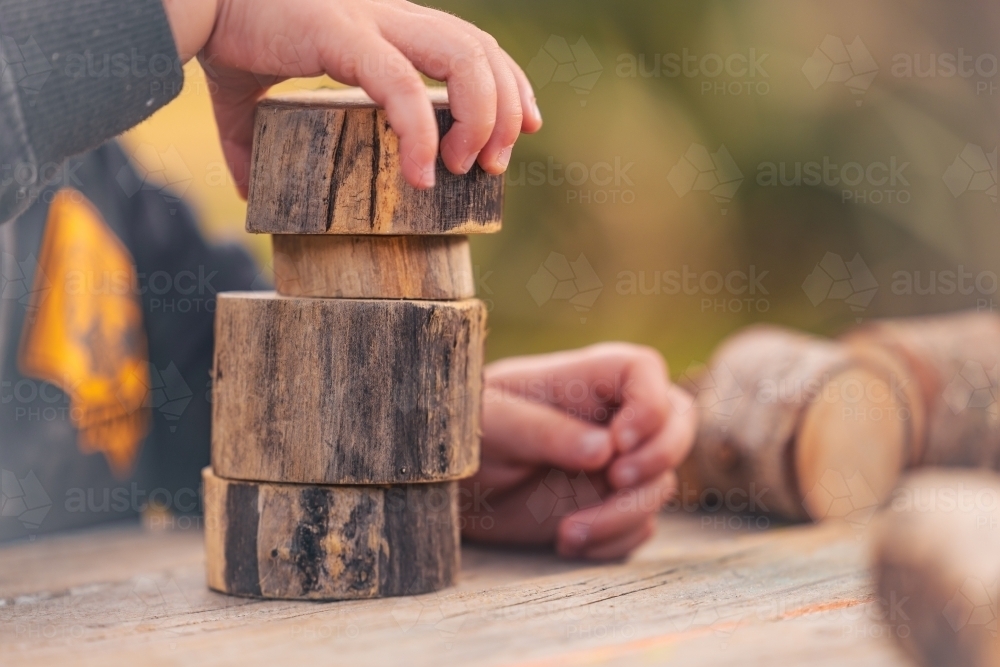 Toddlers hands building tower with natural wooden blocks at preschool - Australian Stock Image