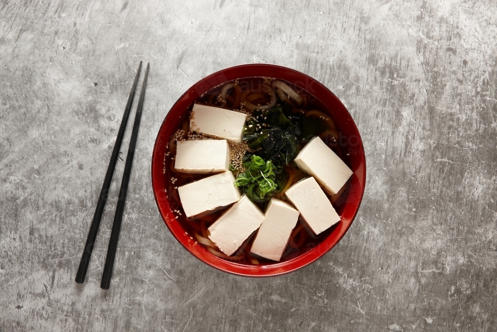 Tofu and noodle soup in red bowl - Australian Stock Image