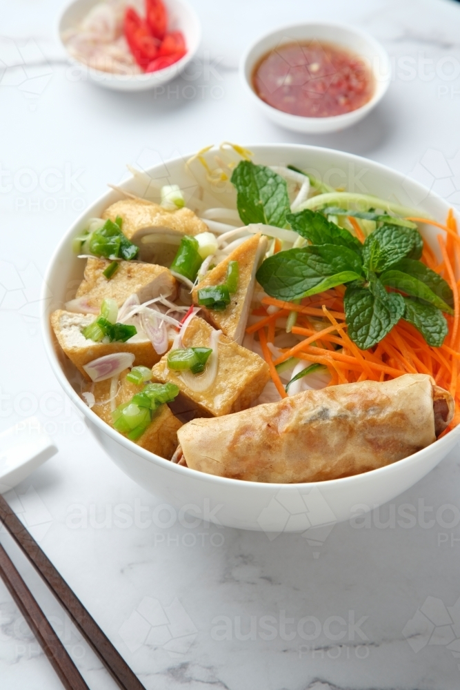 Tofu noodle salad topped with fried lumpia with salad dressing and chopsticks on the side. - Australian Stock Image
