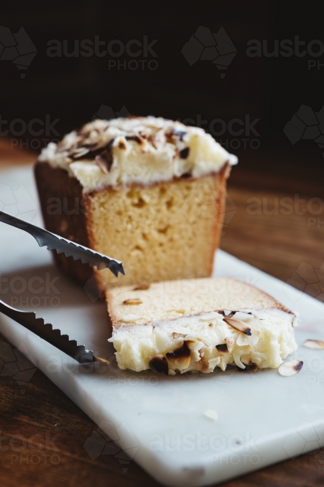 Tongs ready to serve a piece of delicious almond cake vertical - Australian Stock Image