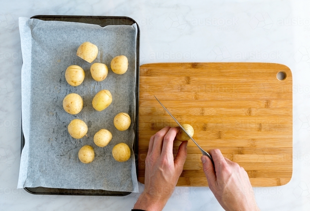 Top down of hands carefully slicing potatoes on bamboo chopping board - Australian Stock Image