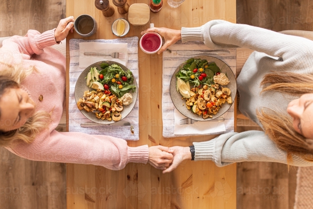Top down shot of two women  holding hands across the dinner table - Australian Stock Image