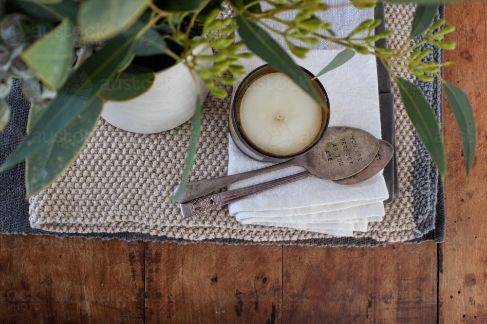 Top down view of table arrangement with flowers, knitted table runner, candle and antique spoons - Australian Stock Image