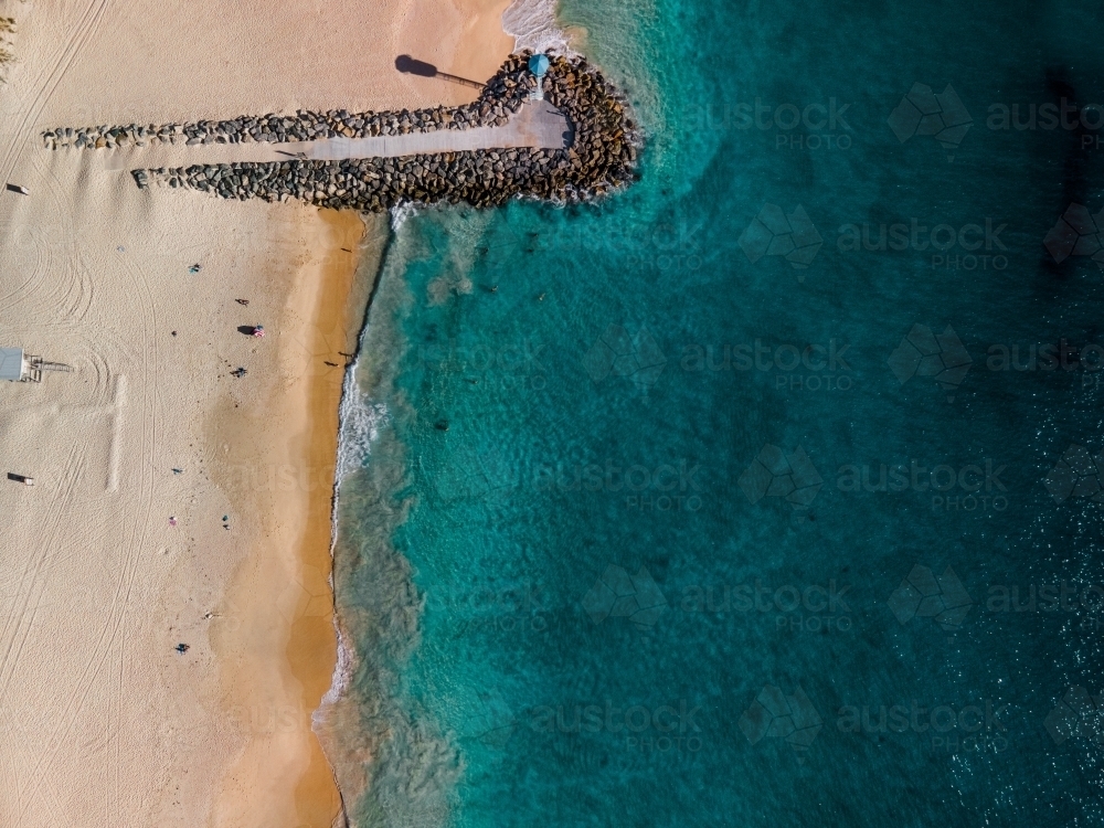 top shot of a beach front with a small walkway made of rocks, lamp post and white sand shoreline - Australian Stock Image