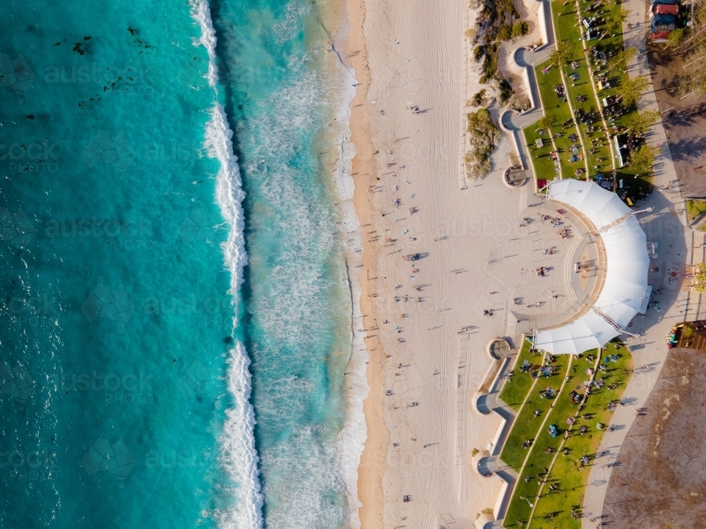 top shot of a beach with waves, white sand, people swimming, grass, trees and buildings - Australian Stock Image