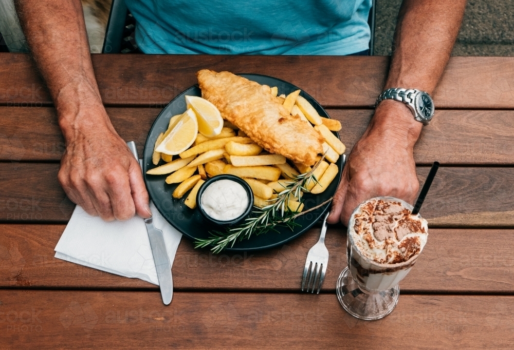 Top view of a man having his plate of fish and chips with a glass of milkshake - Australian Stock Image